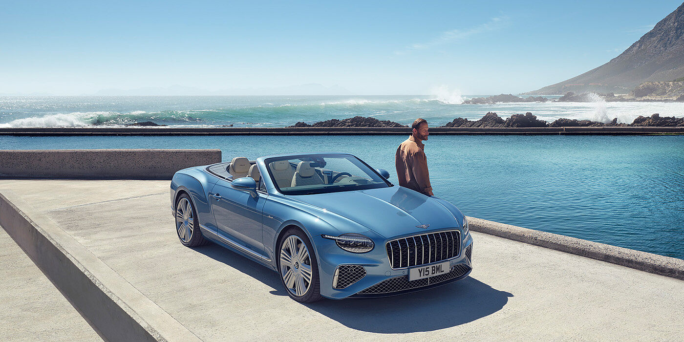Bentley Kyiv New Bentley Continental GTC Azure convertible front view in Light Windsor blue paint with 22 inch ten spoke wheels parked by the sea in the sunshine