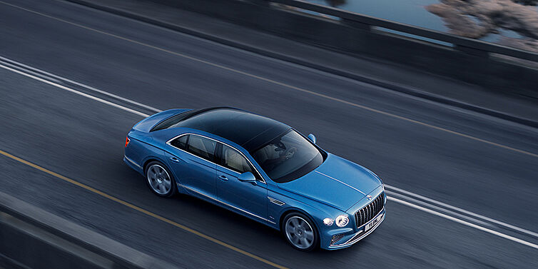 Bentley Kyiv New Bentley Flying Spur Azure sedan in Light windsor blue paint by Mulliner, with 22 inch Azure wheels seen from overhead driving dynamically on a country road