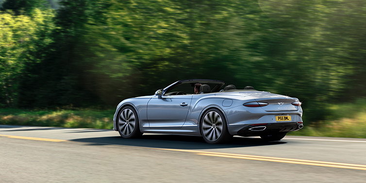 Bentley Kyiv New Bentley Continental GTC convertible side view in Silverlake paint with 22 inch ten spoke wheels driving dynamically on a country road
